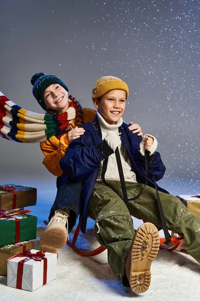 Two children gleefully ride a sled, surrounded by snowfall and holiday gifts, embracing winter fun. — Stock Photo