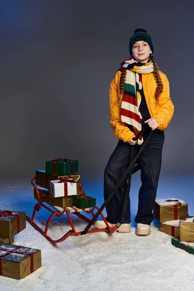 A warmly dressed girl stands by a sled filled with colorful holiday gifts, ready for fun. — Stock Photo