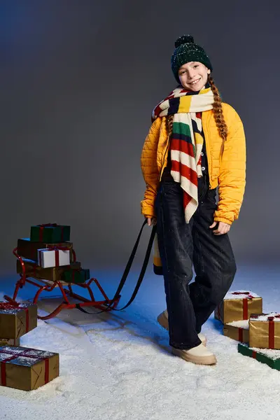 A girl in warm clothes happily pulls a sleigh filled with colorful gifts, capturing winter magic. — Stock Photo