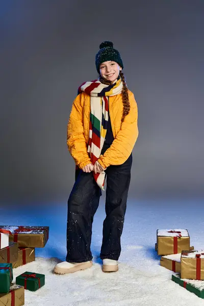 A smiling girl dressed warmly poses with colorful presents in a winter setting. — Stockfoto