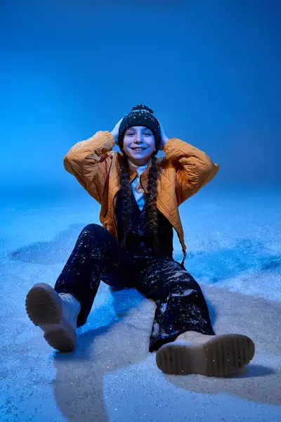 Una ragazza siede felicemente nella neve, indossando vestiti invernali colorati, incarnando la gioia della ragazza. — Foto stock