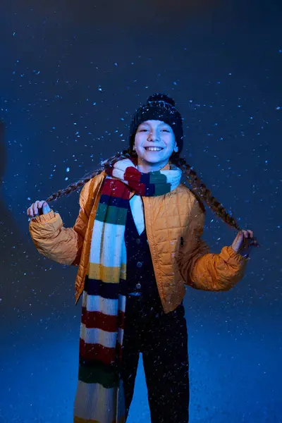 A cheerful girl stands amid gently falling snow, showcasing warm winter clothes with joy. - foto de stock