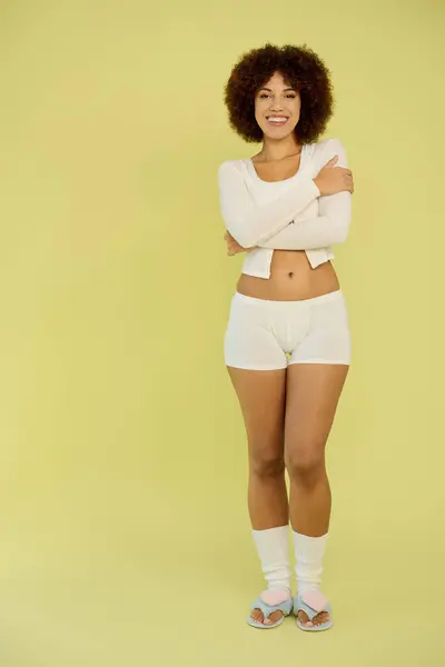 A young African American woman showcases her happiness while standing in underwear on a bright yellow background. — Stock Photo