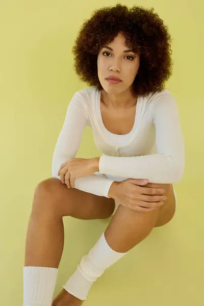 A young woman with curly hair sits gracefully in underwear against a bright backdrop. — Stock Photo