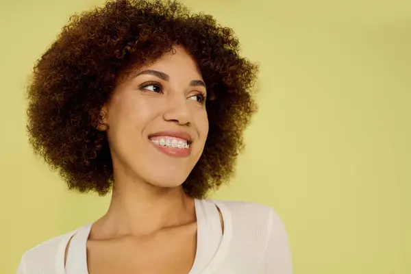 A young woman with curly hair beams with happiness in her underwear against a yellow background. — Stock Photo