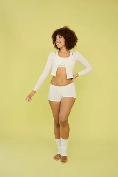 A confident young woman with curly hair poses in stylish underwear against a bright yellow backdrop. — Stock Photo