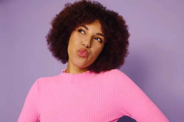 Una joven afroamericana vestida de rosa muestra su emoción juguetona con una expresión confiada. - foto de stock
