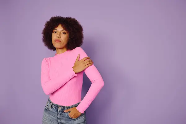 Una joven de color rosa de pie con confianza sobre un fondo púrpura. - foto de stock