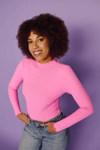 A cheerful young woman with curly hair expresses her emotions while dressed in pink, set against a purple background. — Stock Photo