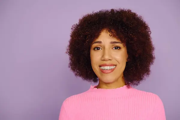 A spirited young woman showcases her happiness while wearing casual pink clothing, set against a purple background. — Stock Photo