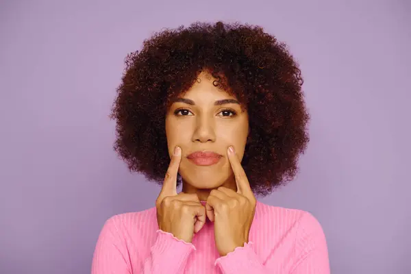 A young African American woman in pink casual wear showcases her emotions creatively against a purple backdrop. — Stock Photo