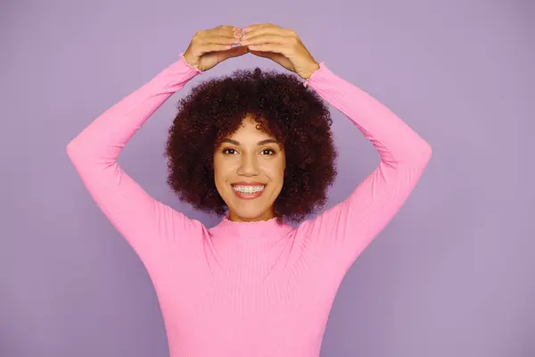 A young woman with curly hair in pink attire joyfully showcases her emotion on a bright purple background. — Stock Photo