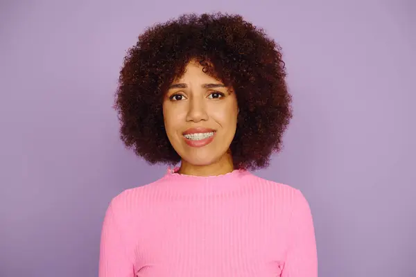 Una mujer joven con el pelo rizado muestra profunda emoción mientras usa atuendo rosa casual en un telón de fondo púrpura. - foto de stock