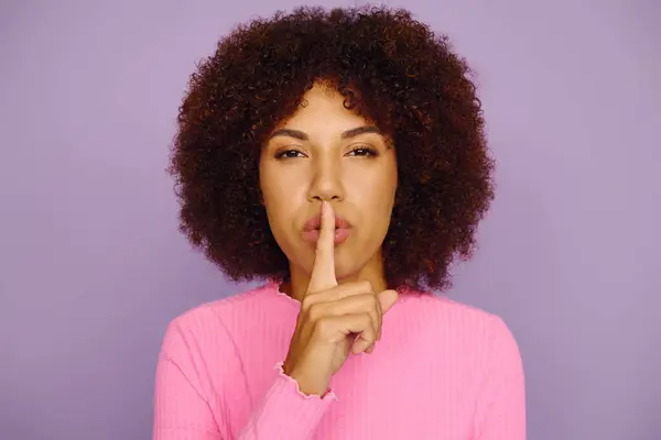 A young Black woman in casual pink conveys deep emotion against a purple backdrop. — Stock Photo
