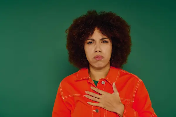 A pretty young woman with curly hair conveys deep emotion while dressed casually against a green backdrop. — Stock Photo
