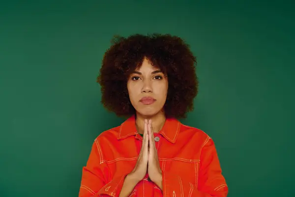 A young African American woman with curly hair conveys strong feelings while standing before a green background. — Stock Photo