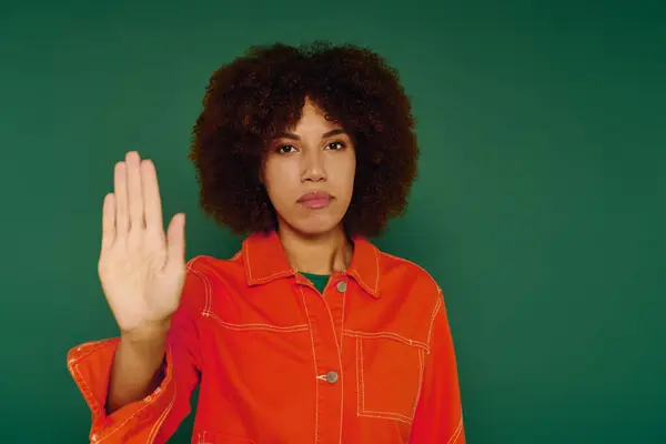 This young African American woman with curly hair showing stop gesture while dressed casually on a green backdrop. — Stock Photo