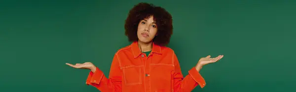 Una giovane donna vivace con i capelli ricci mostrando gesto scrollata di spalle mentre indossa un abito casual in colori vivaci. — Foto stock