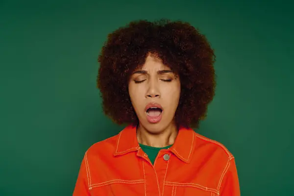 A pretty young woman with curly hair yawning while dressed casually in a bright setting. — Stock Photo