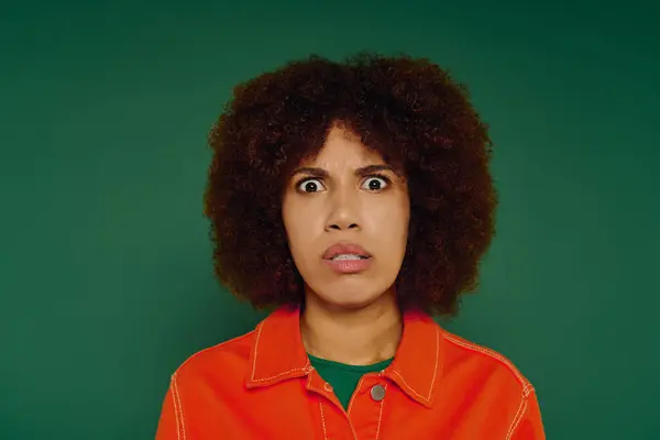 Uma jovem afro-americana mostra surpresa em seu rosto, vestida casualmente contra um pano de fundo verde. — Fotografia de Stock