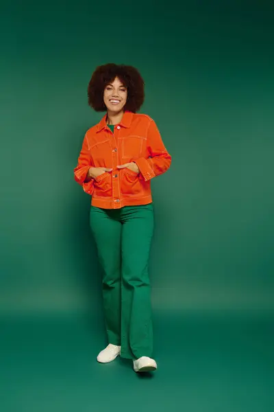 A cheerful young woman showcases her vibrant personality while standing confidently in front of a green backdrop. — Stock Photo
