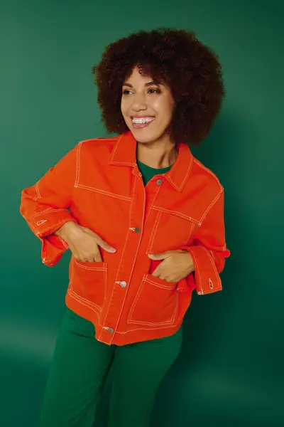 A young woman with curly hair beams brightly in casual clothing, radiating happiness on a lively green background. — Stock Photo