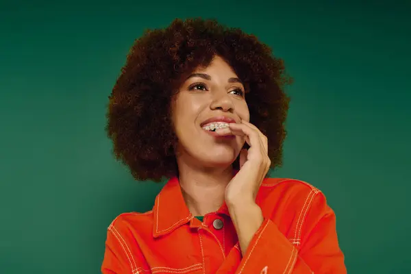 A cheerful young African American woman wearing casual attire shares her joyful emotions amidst a green backdrop. — Stock Photo