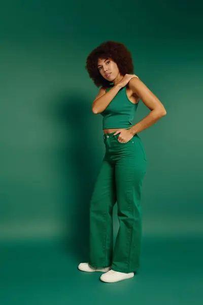 Una giovane donna mette in mostra il suo stile in abiti casual, in piedi con fiducia su uno sfondo verde. — Foto stock
