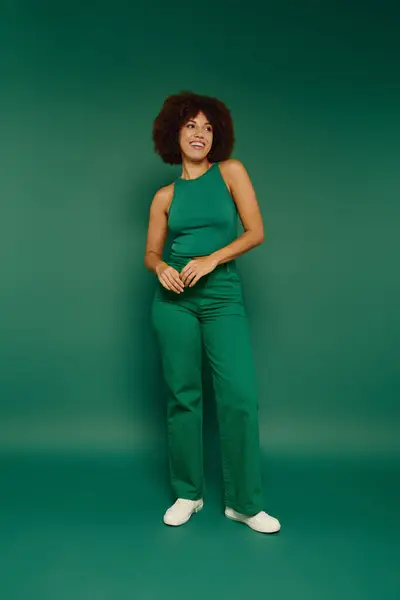 Una giovane donna afroamericana con i capelli ricci irradia gioia mentre si trova su uno sfondo verde vibrante. — Foto stock