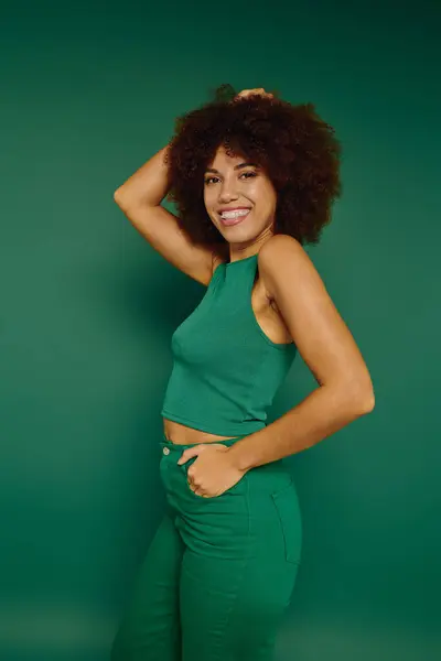 A cheerful young woman with curly hair enjoys a playful moment in casual attire against a vivid green background. — Stock Photo