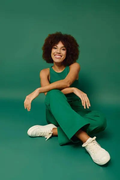 Uma jovem alegre com cabelo encaracolado expressa sua alegria enquanto sentada em trajes confortáveis em um fundo verde. — Fotografia de Stock