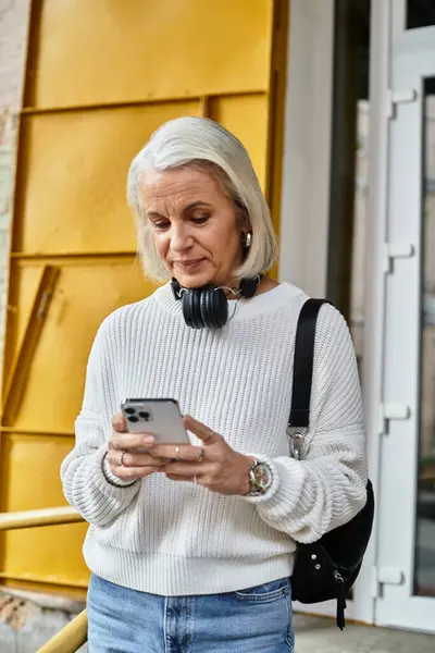 A beautiful gray haired woman engages with her smartphone, surrounded by vibrant colors. — Stock Photo