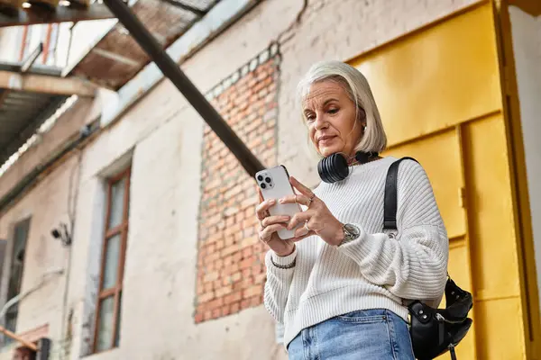 A confident woman with gray hair engages with her smartphone while wearing casual attire. — Stockfoto