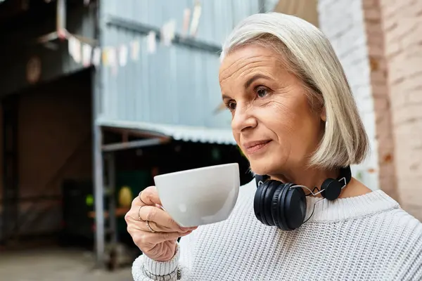 A mature woman with graceful gray hair savors a warm cup of coffee, lost in thought. — Stock Photo