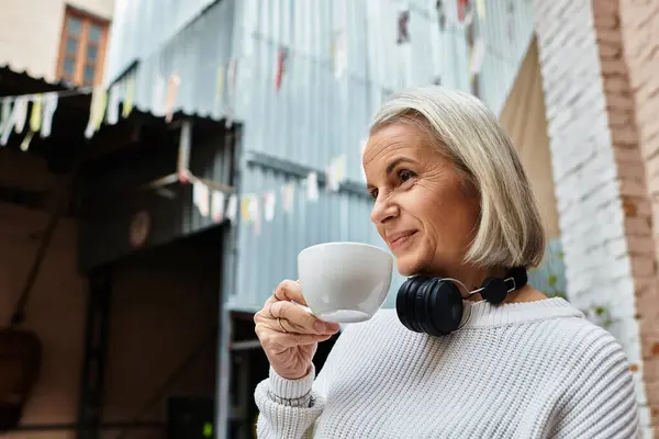 A mature woman with gray hair sips coffee and embraces a moment of relaxation outdoors. — Stock Photo