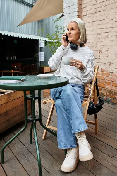 Uma bela mulher madura sorve café e bate-papos em seu telefone enquanto sentado ao ar livre. — Fotografia de Stock