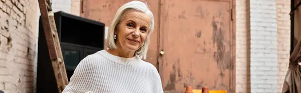 Una mujer madura sonríe calurosamente mientras se dedica a una actividad artística rodeada de texturas urbanas. - foto de stock