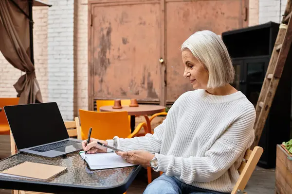 A lovely mature woman with gray hair writes notes at a tranquil outdoor table. — Stock Photo