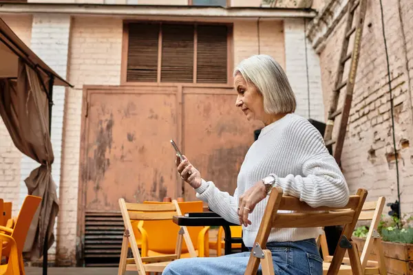 A mature woman with beautiful gray hair sits comfortably in a cafe, engaged with her smartphone. — стоковое фото