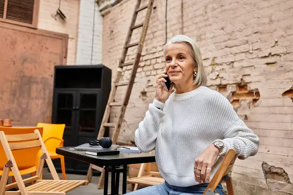 A beautiful mature woman is engaged in a cheerful phone conversation while seated comfortably. — Stock Photo