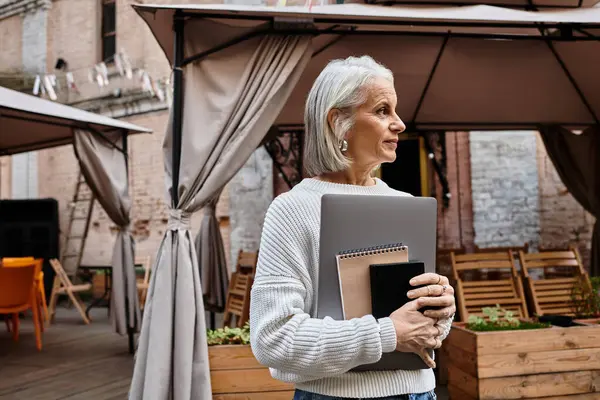 A mature woman with silver hair holds notebooks as she enjoys a relaxed moment outdoors. — стоковое фото