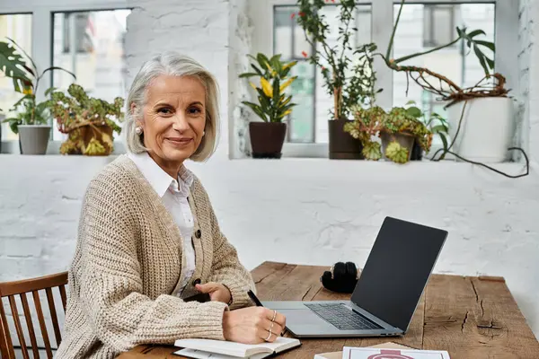 A graceful mature woman takes notes while enjoying the tranquil atmosphere of her workspace. — Stock Photo