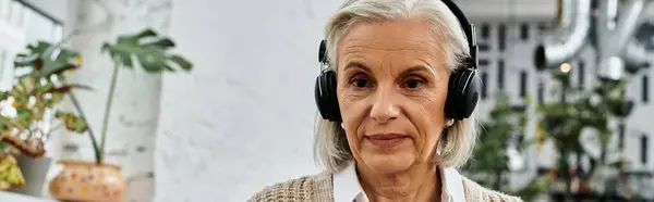 A mature woman with beautiful gray hair immerses herself in music while surrounded by lush greenery. — Stock Photo