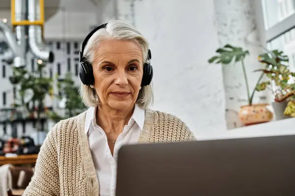A mature woman with gray hair listens attentively during her virtual gathering in a warm atmosphere. — Stock Photo