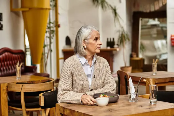 A gray haired woman enjoys her meal alone at a wooden table in a cozy setting. — Stock Photo