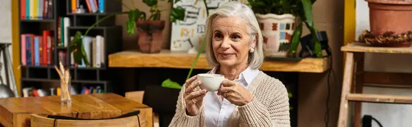 A beautiful woman with gray hair sips her drink while relaxing in a charming environment. — Stock Photo