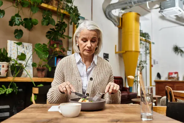 A mature woman with gray hair savors a nutritious dish at a cozy urban cafe. — Stock Photo