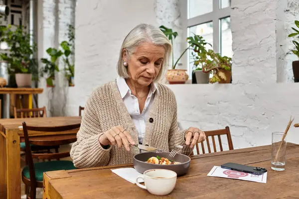 A beautiful woman with gray hair is savoring her meal in a plant filled cafe. — Stock Photo