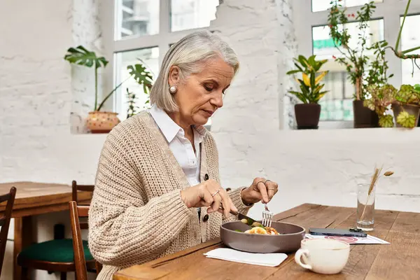 A beautiful older woman sits at a wooden table savoring her delicious meal. — Stock Photo