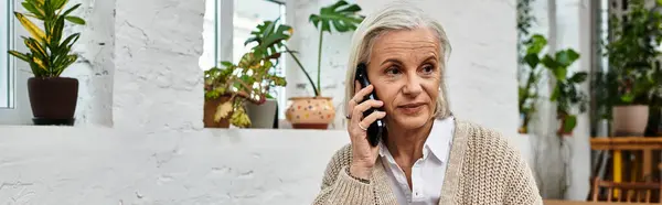 A beautiful mature woman engages in a phone conversation while surrounded by plants. — Stock Photo